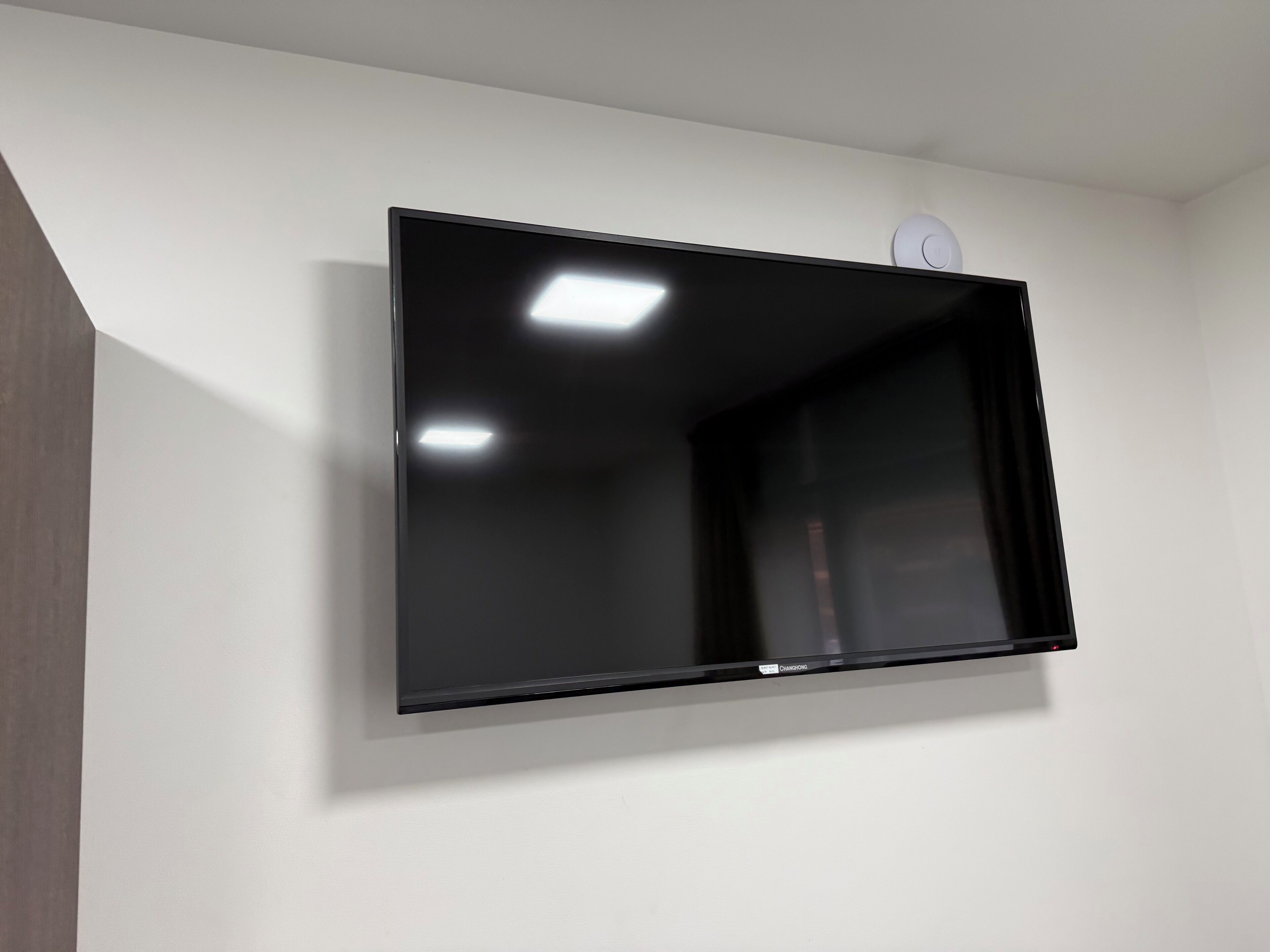A flat-screen TV mounted on a white wall with a ceiling light fixture above it.