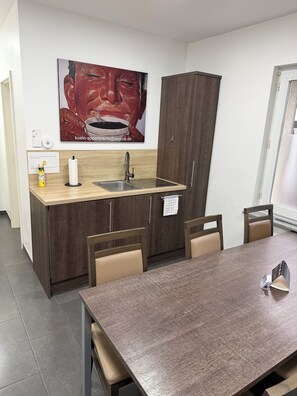 Eine kleine Küche mit Holzarbeitsplatte, Spüle und Schrank. Ein Esstisch mit Stühlen und ein Poster an der Wand.