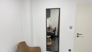 Une pièce moderne avec un fauteuil marron, une table en verre, un grand miroir et une porte blanche.