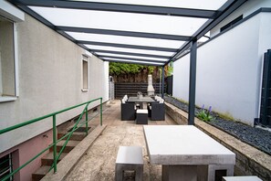 Ein überdachter Patio-Bereich mit Tisch und Stühlen, einer Betonbank und einer Treppe.
