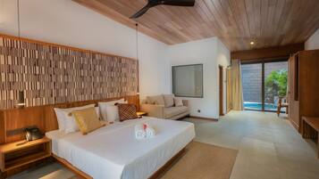 Quarto de hotel moderno com uma cama grande, um ventilador de teto, cabeceira de madeira, sofá, televisão e uma porta de vidro deslizante para uma área de piscina.