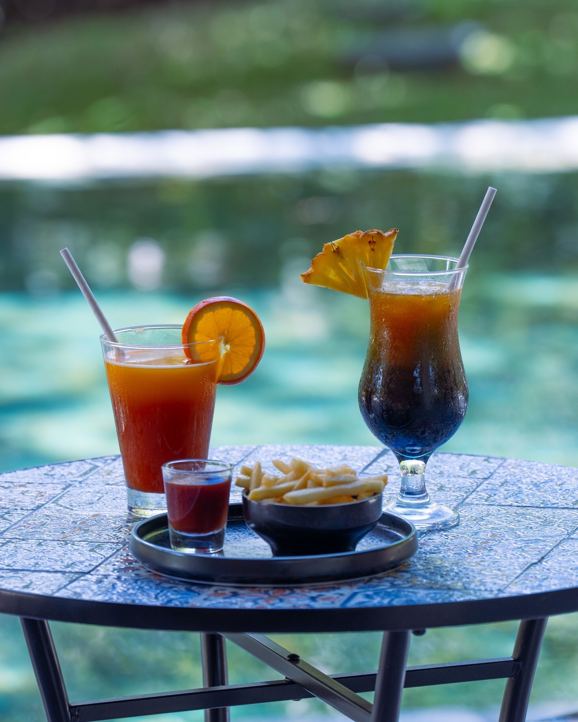 A table with two drinks, a small bowl of fries, and a glass of ketchup.
