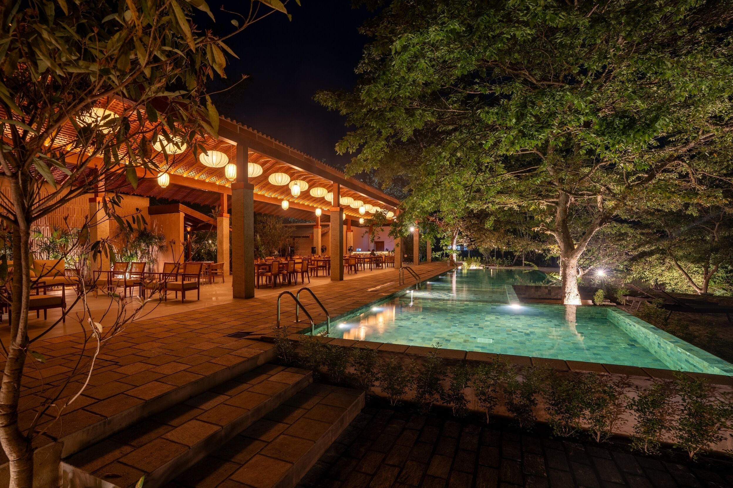 A poolside area with a covered seating area, steps leading to the pool, and a tree in the background.