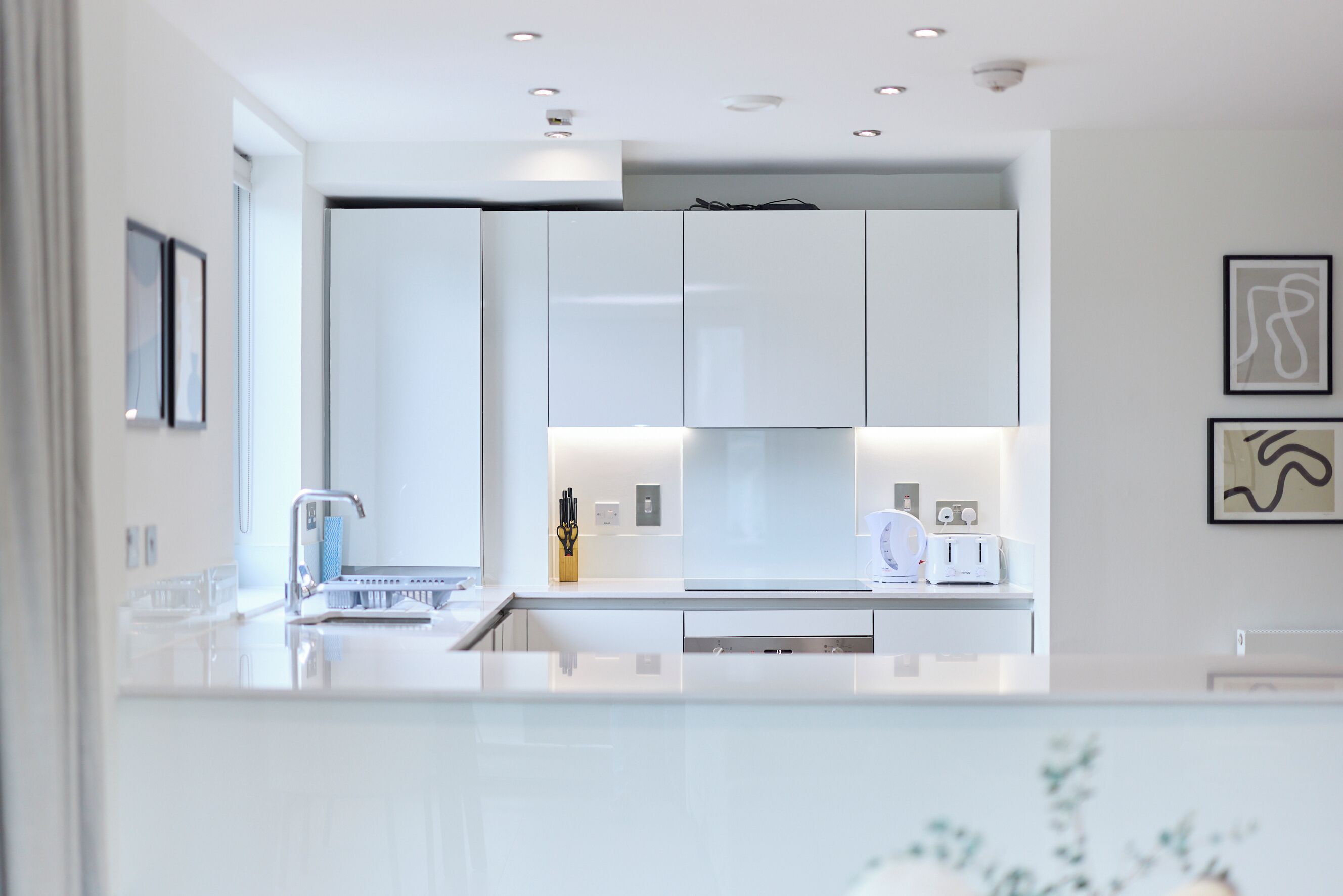Een moderne keuken met witte kasten, een roestvrijstalen spoelbak en een aanrecht met een broodrooster en andere apparaten.
