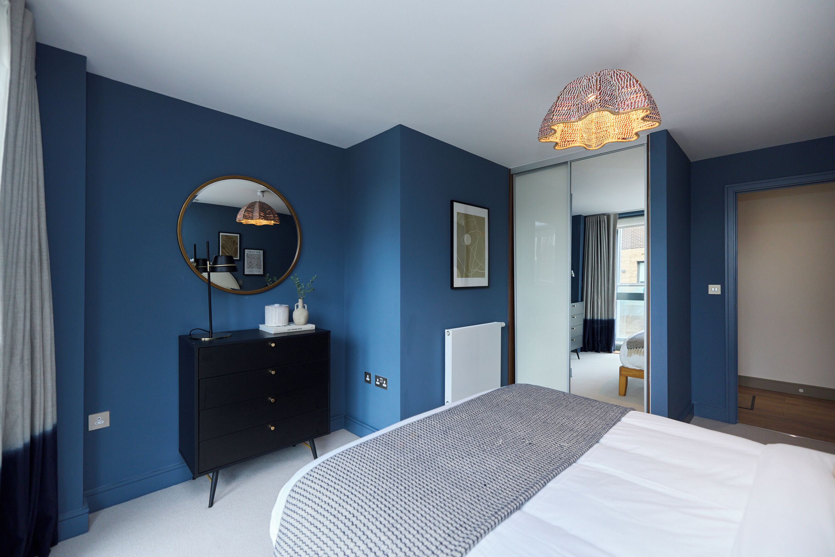 A bedroom with a large bed, a dresser, a mirror, and a unique ceiling light fixture.