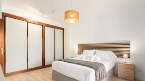 Ein modernes Schlafzimmer mit einem großen Bett, einem Holzkopfteil, Nachttischen und einem Schiebetürenschrank.
