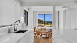 A modern kitchen with white cabinetry, a black faucet, and a view of the sea through large windows. - Fishers - Scenic Drive 35 (Bermagui)