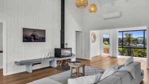 A modern living room with a fireplace, a sofa, and a view of the outdoors. - Fishers - Scenic Drive 35 (Bermagui)