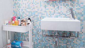Ein Badezimmer mit einer wandförmigen Fliesenmosaik, einem weißen Waschbecken mit Spiegel darüber, einer weißen Toilette, einem Mülleimer und einem weißen Aufbewahrungswagen mit Toilettenartikeln.