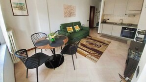 En kompakt opholdsstue med spiseplads, en grøn sofa, et køkken og en radiator.