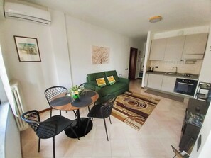 A compact living space with a dining area, a green sofa, a kitchen, and a radiator. - APARTMENT IN A STATELY SETTING.  SUITABLE FOR COUPLE OR FAMILY WITH CHILDREN (Como)