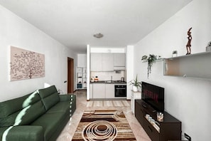 A modern living room with a green sofa, a flat-screen TV, and a kitchen in the background. - APARTMENT IN A STATELY SETTING.  SUITABLE FOR COUPLE OR FAMILY WITH CHILDREN (Como)