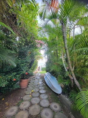 A pathway lined with potted plants and a blue kayak, leading to a garden area.