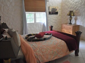 Une chambre à coucher comprenant un lit, une table de chevet, une commode, une fenêtre avec des rideaux et une lampe fixée au mur.