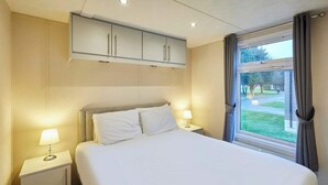Ein Hotelzimmer mit einem Bett, zwei Nachttischen mit Lampen, einem Fenster mit Vorhängen und einem an der Decke befestigten Schrank.