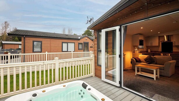 Ein Whirlpool auf einer Holzterrasse mit einer Glastür zu einem Wohnbereich, der eine Couch und einen Fernseher beinhaltet.