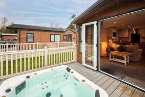 Un jacuzzi en una terraza de madera con una puerta de vidrio que da a una sala de estar con un sofá y un televisor.