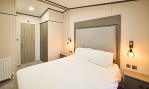 Ein Hotelzimmer mit einem großen Bett, zwei Nachttischen, einer Wandleuchte und einer Holztür.
