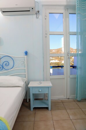 Une chambre à coucher comprenant un lit, une table de chevet, une fenêtre donnant sur des immeubles et un appareil de climatisation.