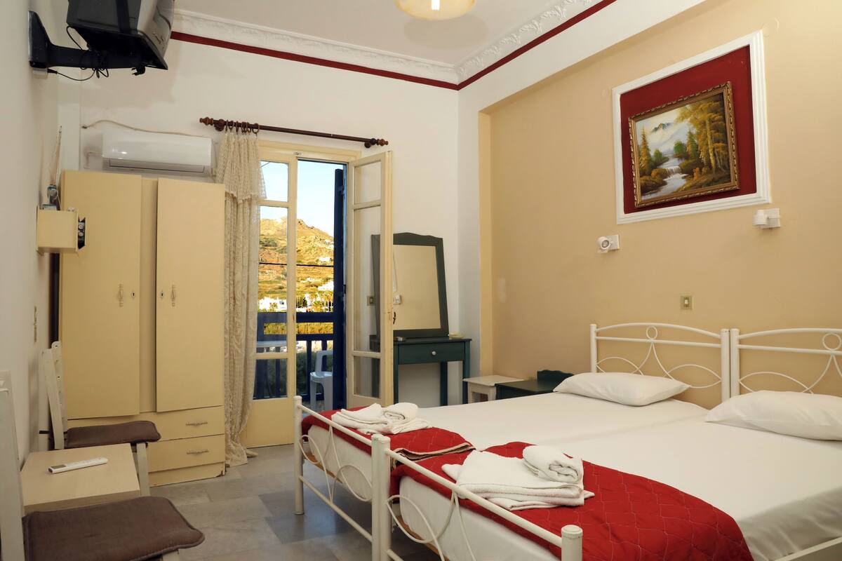 Une chambre d’hôtel équipée d’un lit, d’un bureau, d’une armoire et d’une fenêtre donnant sur des arbres.