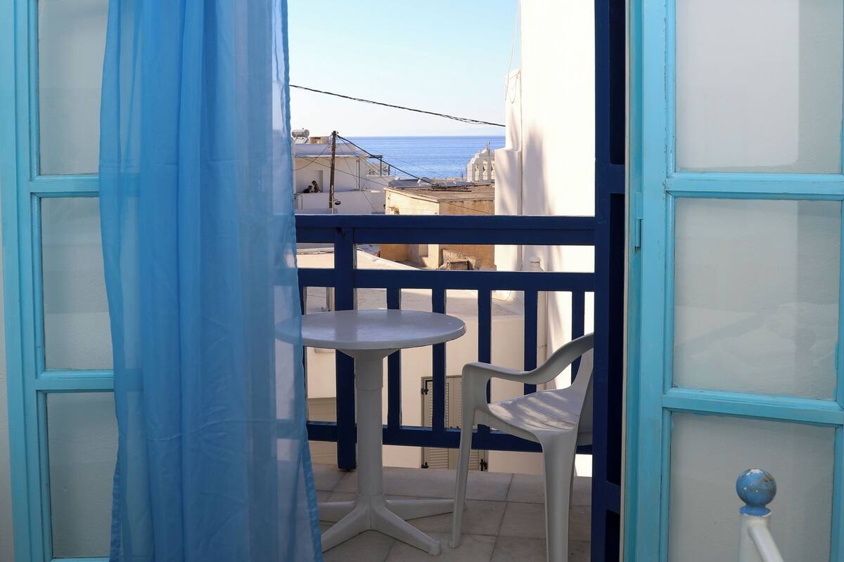 Une pièce comprenant un lit, une table et une chaise, avec vue sur la mer par une porte ouverte.