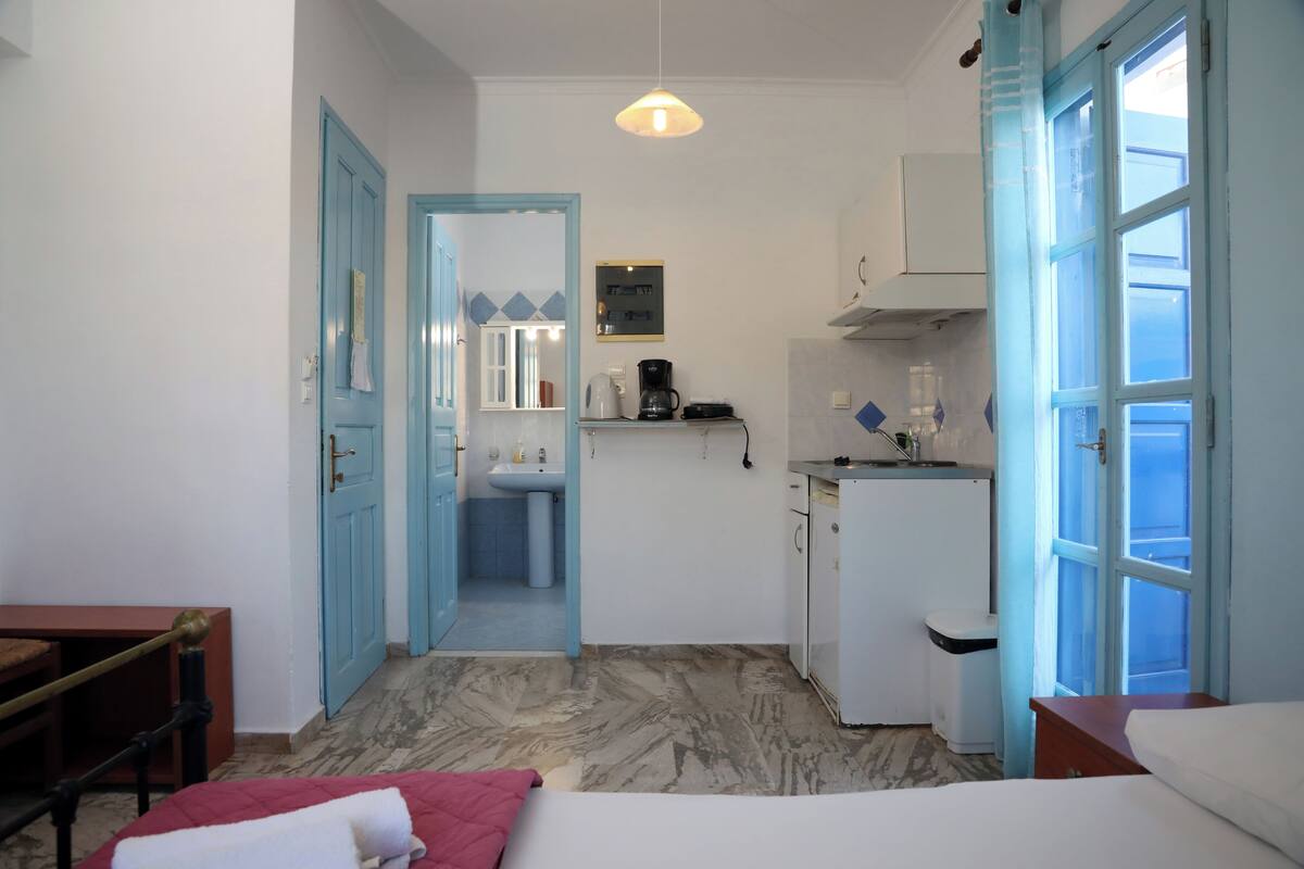 Une pièce de taille modeste comprenant un lit, un bureau, une petite kitchenette et une salle de bain visible par une porte ouverte.