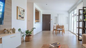 A modern living room with a wooden floor, a dining area with a table and chairs, a bookshelf, and a large window. - Modern 3BR retreat for 6 at Tucan Country Club ⛳🌿 Enjoy golf views, resort-style living, and peaceful nature surroundings just minutes from Panama City. Perfect for families, friends, or business stays seeking comfort and privacy. ✨ (Cocoli)