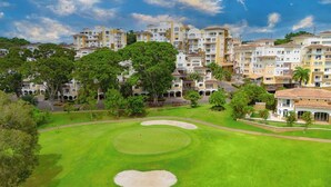 A golf course with a sand bunker, surrounded by multi-story residential buildings. - Modern 3BR retreat for 6 at Tucan Country Club ⛳🌿 Enjoy golf views, resort-style living, and peaceful nature surroundings just minutes from Panama City. Perfect for families, friends, or business stays seeking comfort and privacy. ✨ (Cocoli)