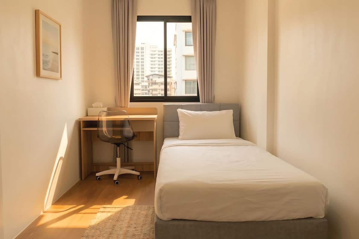 Ein kleines, ordentlich eingerichtetes Schlafzimmer mit einem Bett, einem Schreibtisch und einem Stuhl.