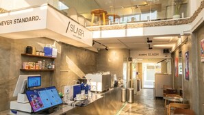 A cafe with a modern interior, a cash register, and a sign that reads 'SLASH CAFE & BARBY.'