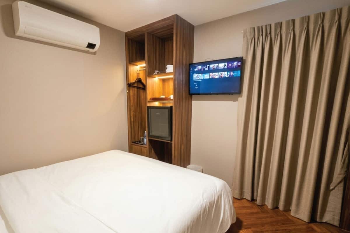 Ein Hotelzimmer mit einem Bett, einem an der Wand montierten Fernseher, einem Kleiderschrank und einem Vorhang.