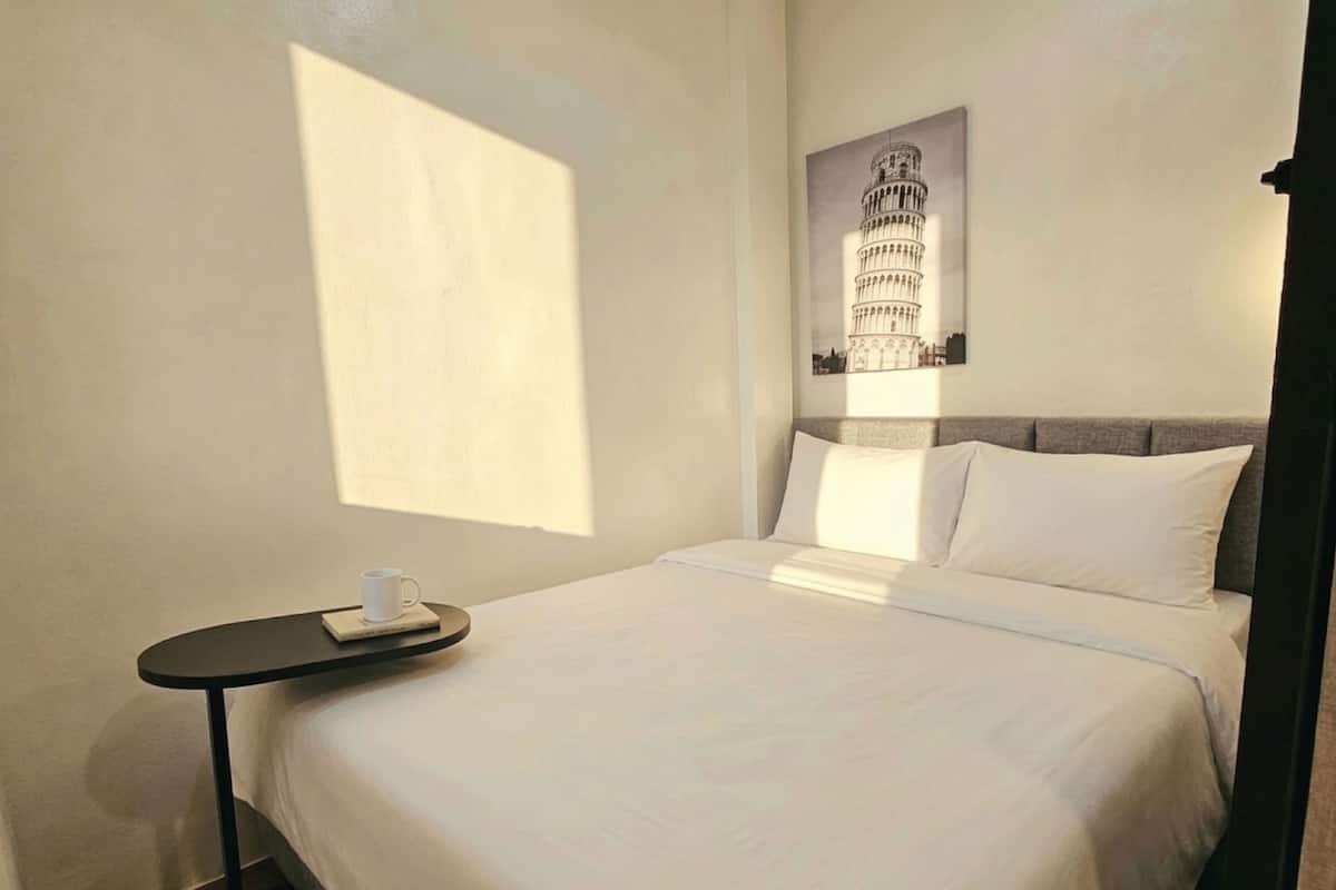 Ein Hotelzimmer mit einem Bett, einem kleinen Tisch mit einer Tasse, einem Kopfkissen und einem Wandbild mit dem Schiefen Turm von Pisa.