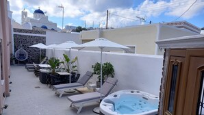 A rooftop lounge with lounge chairs, umbrellas, and a hot tub. - Navita Cave Houses (Santorini)