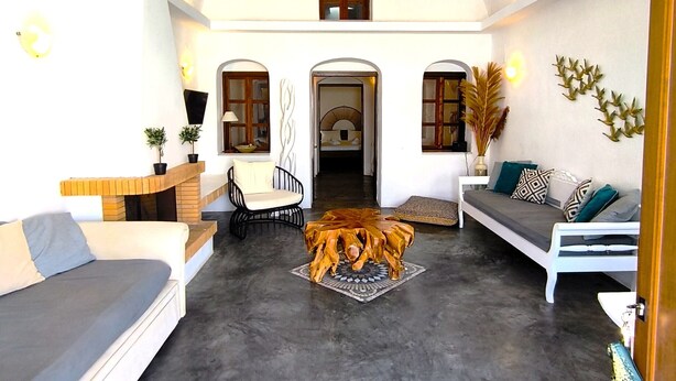 A spacious living area with a high ceiling, a built-in fireplace, and a cozy seating arrangement including a sofa and a chair. - Navita Cave Houses (Santorini)