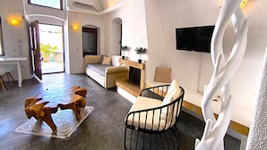 A modern living room with a sofa, a dining table, and a TV mounted on the wall. - Navita Cave Houses (Santorini)