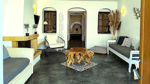 A spacious living area with a high ceiling, a fireplace, and a large wooden coffee table. - Navita Cave Houses (Santorini)