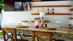 Eine Bar mit einer Steintheke, Holzstühlen und einem an der Wand befestigten Fernseher.