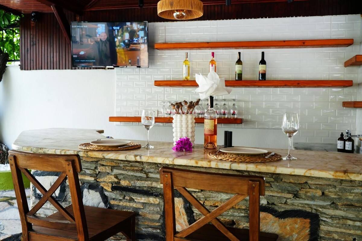 A bar area with a stone counter, wooden chairs, and a TV mounted on the wall.