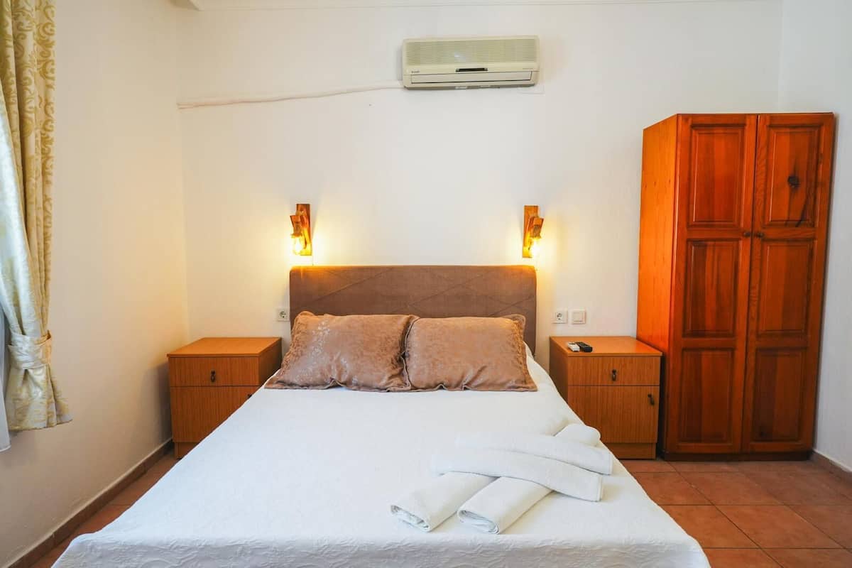 A bedroom with a bed, two bedside tables, a wardrobe, and an air conditioning unit on the wall.
