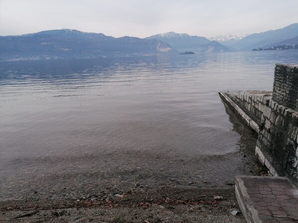 A calm lake with mountains in the background and a stone wall on the right.