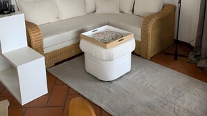 Una sala de estar con sofá, reposapiés y una mesita con bandeja. En la pared hay cuadros enmarcados, una lámpara de pie y un estante con adornos.