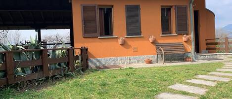 A building with a sloped roof, multiple windows with shutters, a bench, and a paved pathway leading to the entrance.