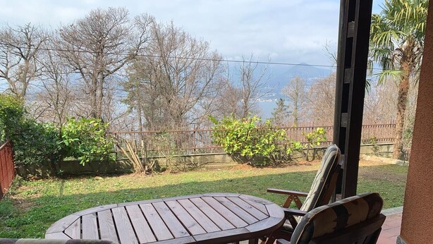 Un patio con una mesa redonda y sillas, vistas a árboles y una masa de agua, y una cerca.