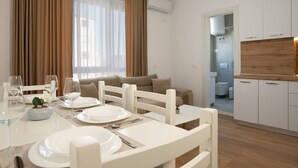Un salon moderne avec un coin repas, des meubles blancs et une cuisine visible à travers une porte ouverte.