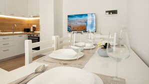 Un espace de repas moderne, avec des meubles blancs, un téléviseur diffusant une image de paysage et une cuisine en arrière-plan.
