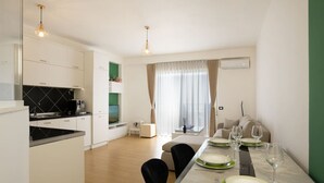 A modern kitchen with white cabinets, a black countertop, and a dining area with a table set for two. - Greenview Apartment by Tok Apartments (Durrës)