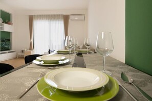 Een eettafel gedekt met borden, glazen en bestek in een kamer met een groene accentmuur en een raam met gordijnen.