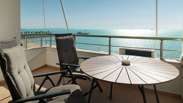 Un balcón con una mesa redonda y dos sillas, con vista al mar y un barco en la distancia.