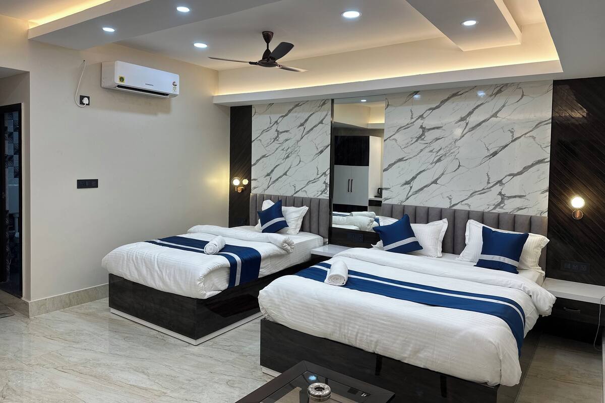 A modern hotel room with two beds, a ceiling fan, recessed lighting, a large mirror, and marble wall accents.