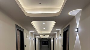 Um corredor longo e bem iluminado, com piso brilhante, iluminação embutida e arandelas.
